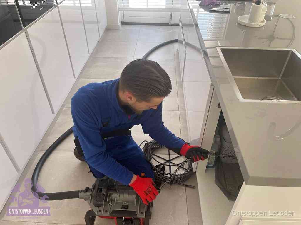 Een monteur ontstopt de keukenafvoer onder de spoelbak met een elektrische veermachine in Leusden