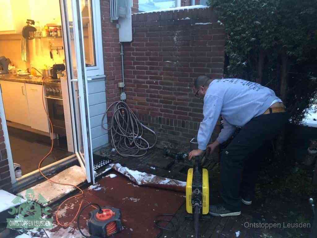 Een monteur werkt buiten bij een open riool-/grondput met een elektrische ontstoppingsmachine om een verborgen afvoerprobleem op te sporen in Leusden