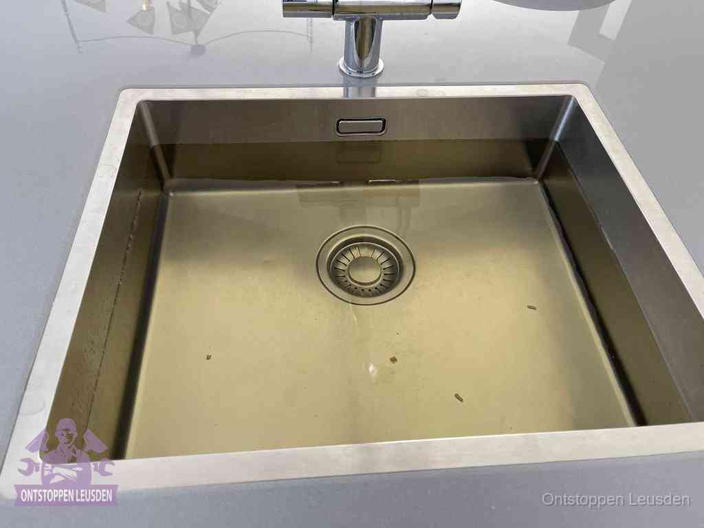 Stilstaand water in een rvs spoelbak dat niet wegloopt, een duidelijk signaal van een gootsteenverstopping in Leusden