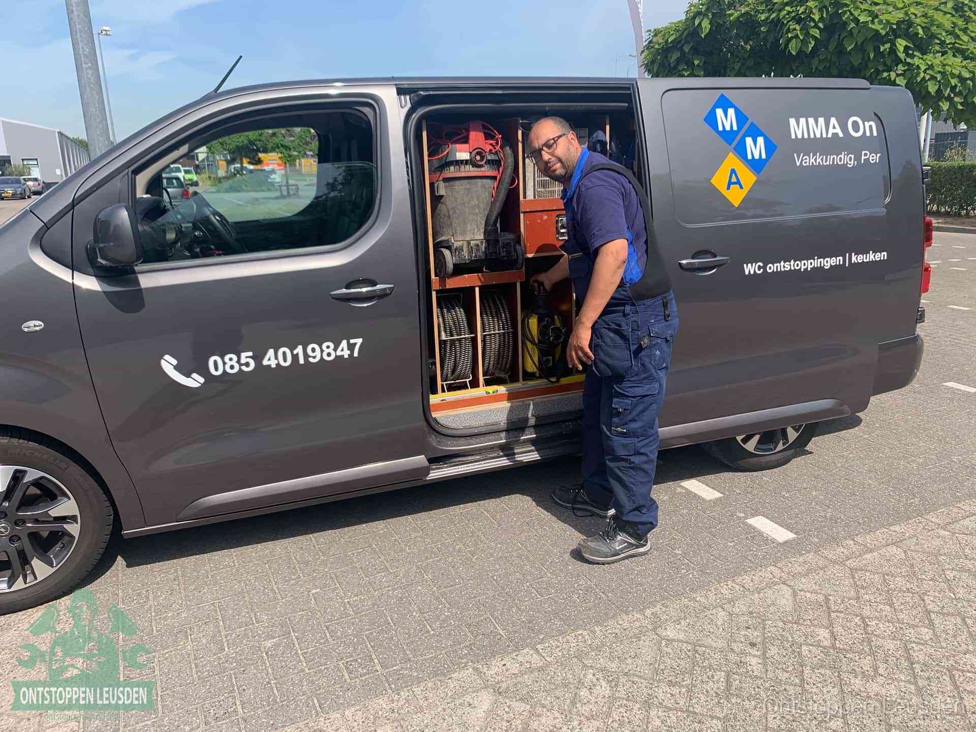 Een monteur bij de open schuifdeur van zijn bedrijfsbus op een parkeerplaats, klaar om de oorzaak van terugkerende afvoerverstoppingen aan te pakken in Leusden
