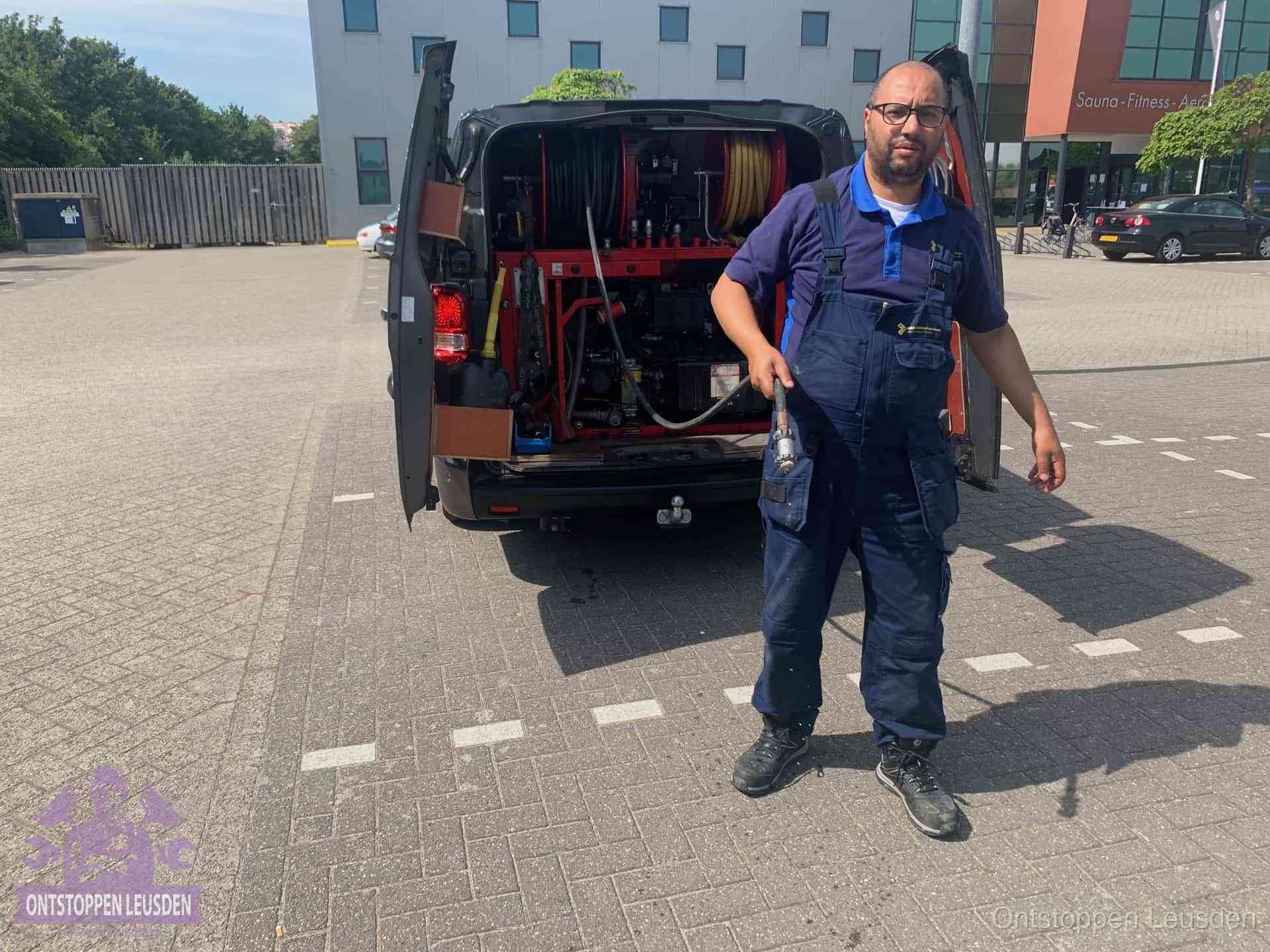 Een monteur bij zijn bestelbus met een hogedruk- en rioolreinigingsunit, klaar om de oorzaak van terugkerende wc-verstoppingen aan te pakken in Leusden