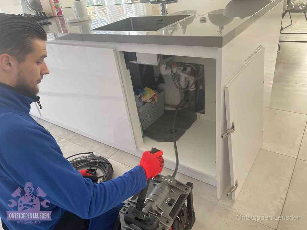 Monteur ontstopt met een veermachine een verstopte afvoer onder de gootsteen in Leusden