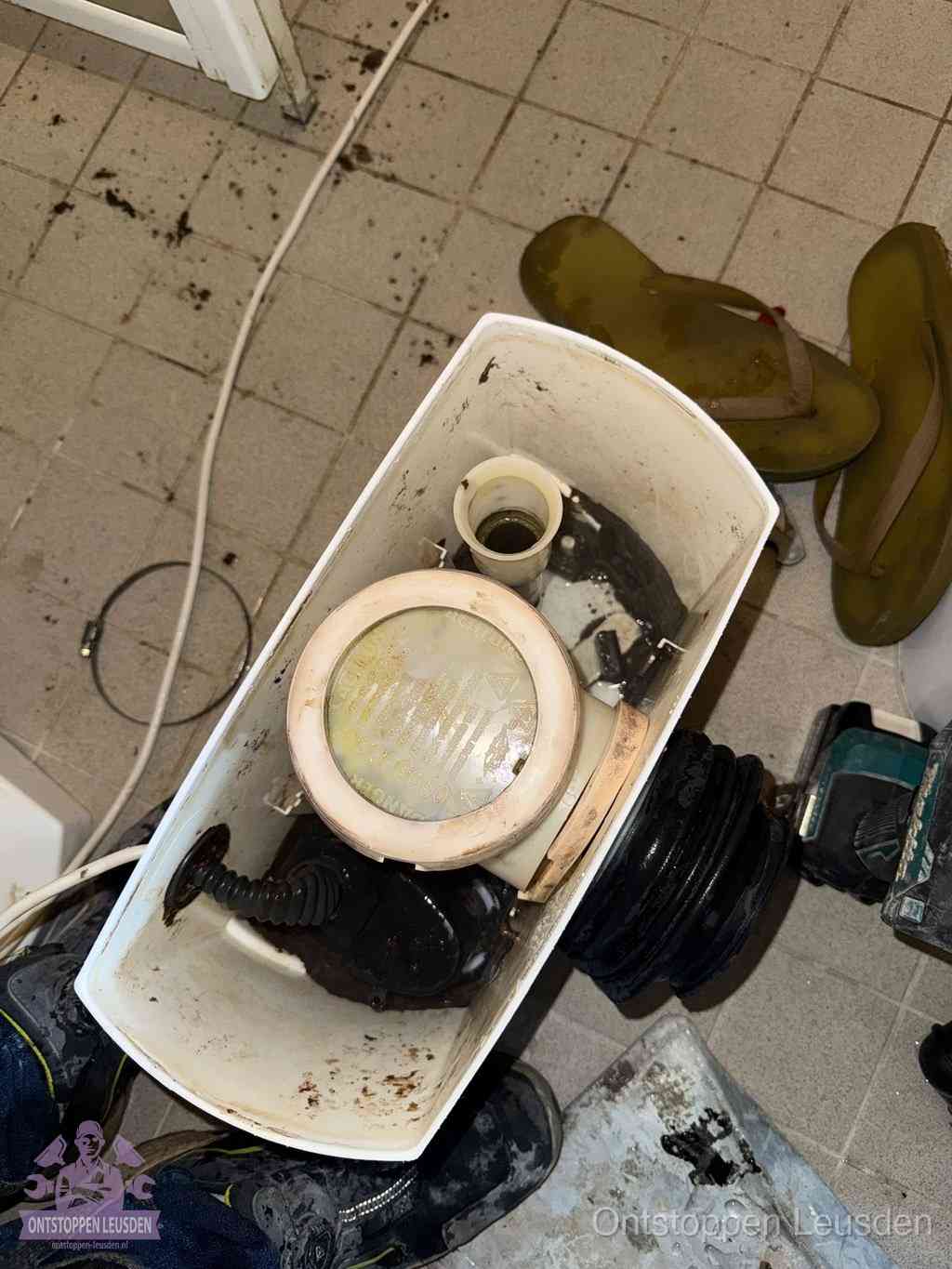 Een gedemonteerde toiletpot op de vloer met ontstoppingsveer en gereedschap ernaast, het verwijderen van een vastzittend voorwerp uit de wc in Leusden