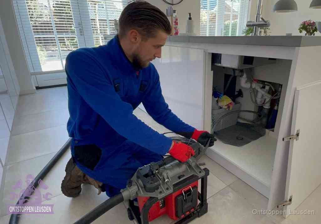 Een monteur voert een professionele elektrische ontstoppingsmachine in de afvoer onder de spoelbak tijdens het gootsteen ontstoppen in Leusden